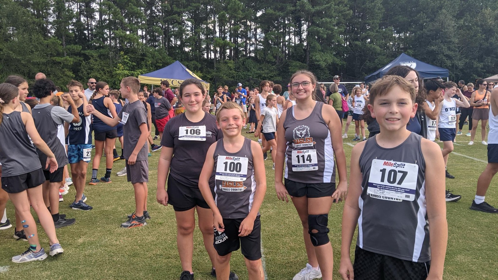 Four Fellowship Christian Academy cross country runners in Eagles jerseys with race bibs, smiling together at a meet