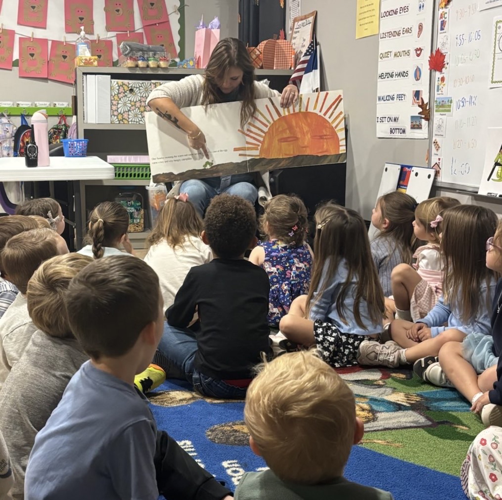 A teacher reads a big picture book to young students gathered on the classroom rug during circle time